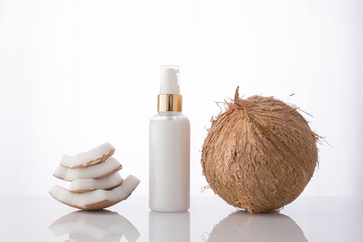 High key homemade cosmetic coconut products with coconut on white background. Lotion cream with coconut stack and green leaf.