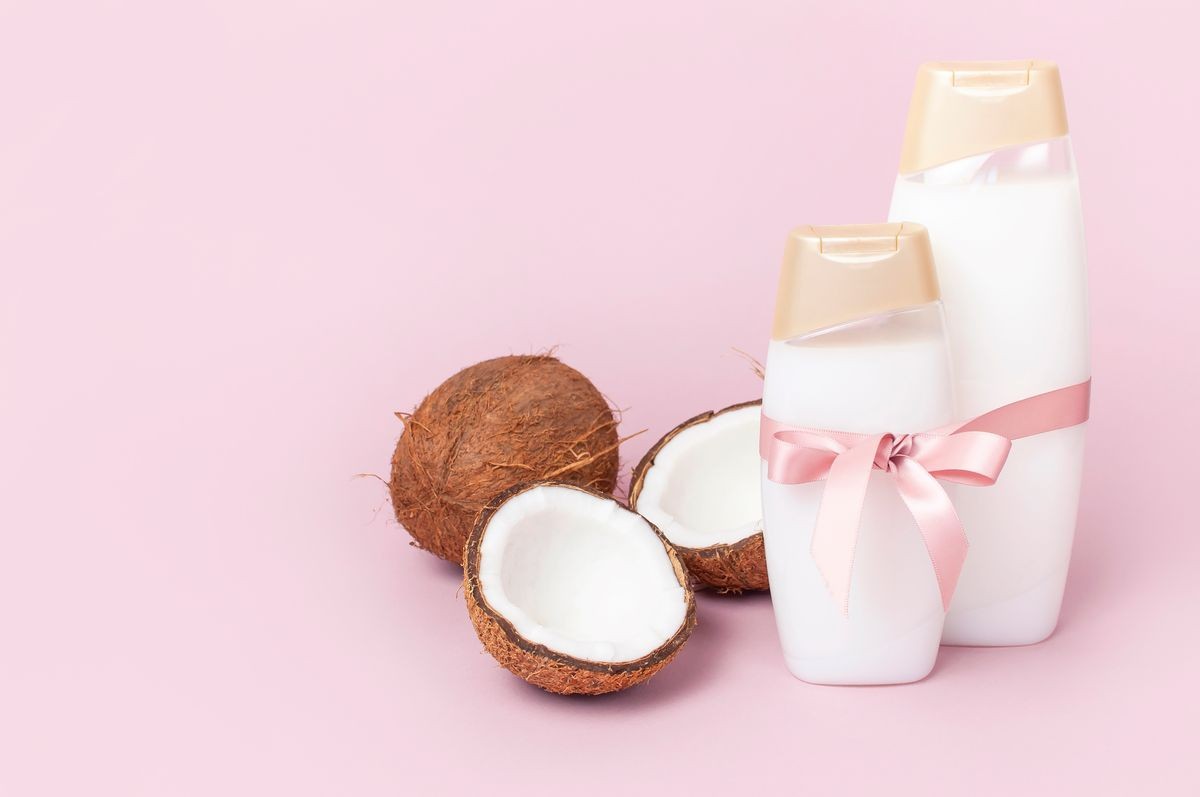 Organic cosmetics with shower gel, ripe coconut on pink colored background minimal flat lay style. Coconut oil, milk. Healthy skincare. Homemade cosmetic for peeling and spa concept. 