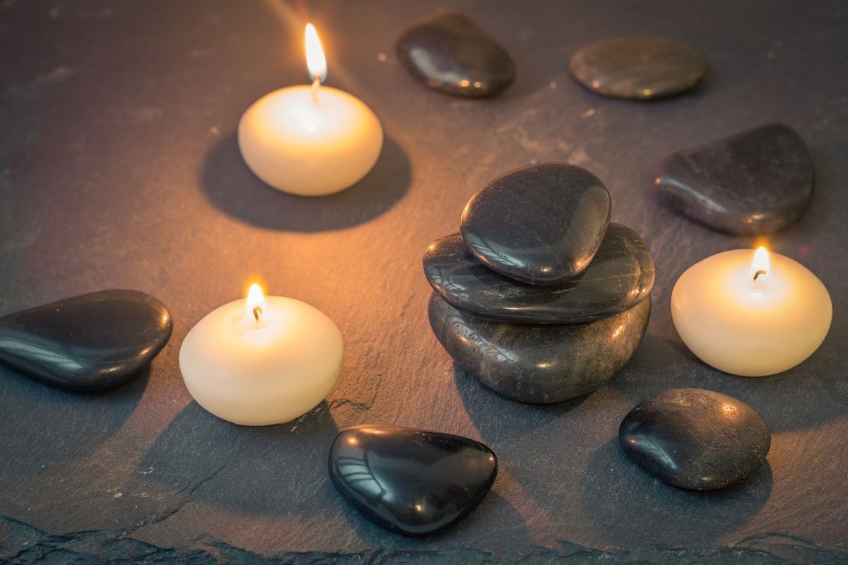 black lava massage stones with burning candles on dark stone surface.