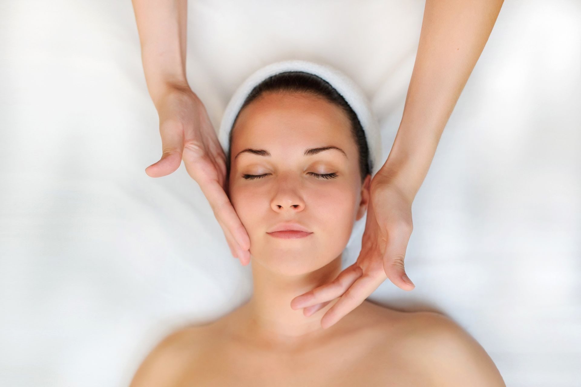 Spa procedure of face massage. Top view. Beautiful young woman lying on back. Masseur /therapist massaging her face