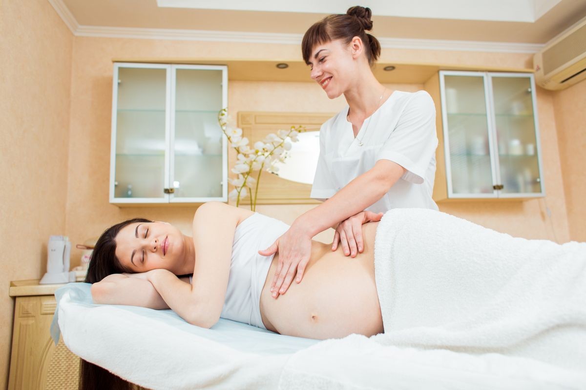 Beautiful young woman doctor massage therapist in a cosmetology room doing a massage to a pregnant girl with long hair